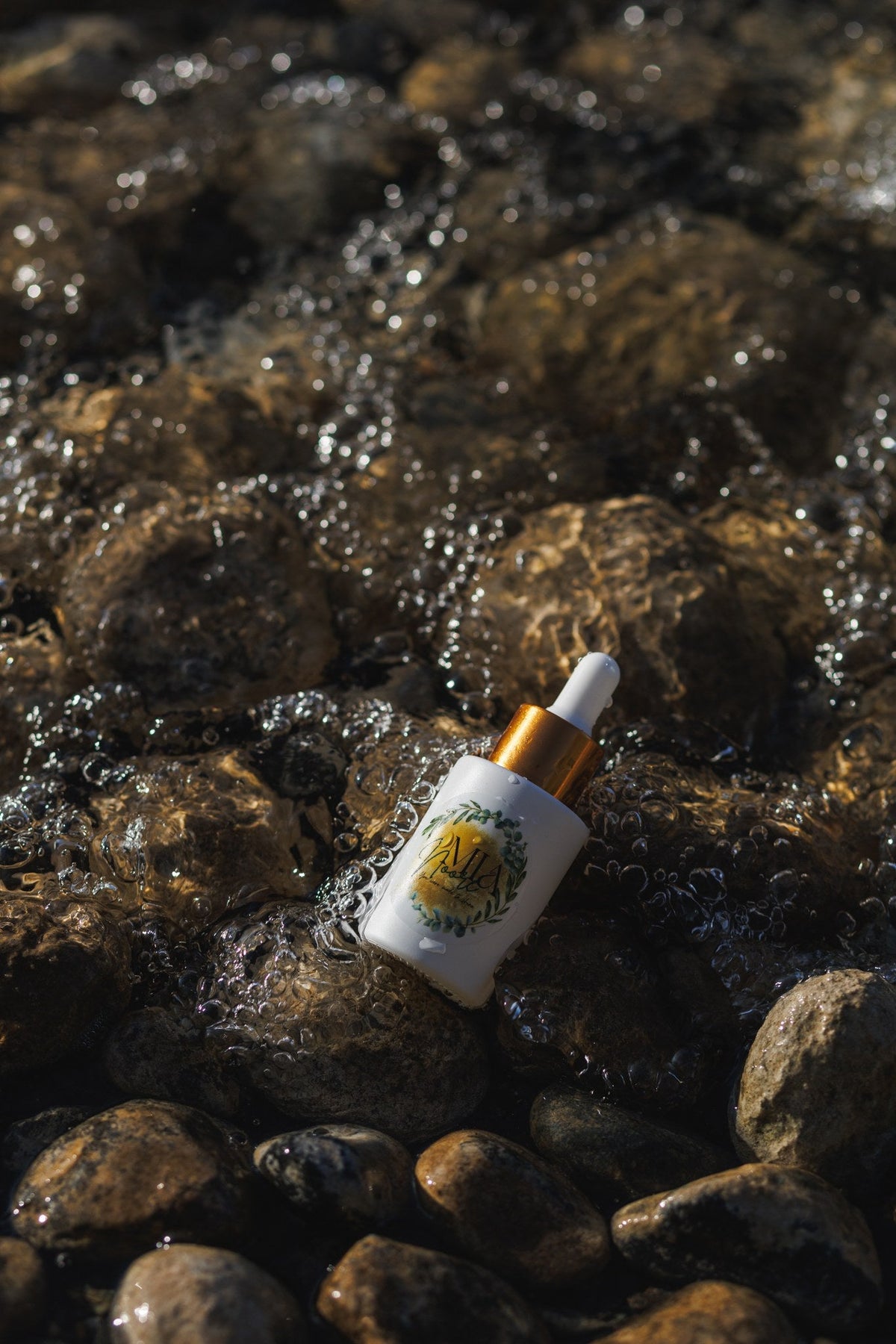 Mia Noore Balanced Harmony face oil bottle resting on wet river stones