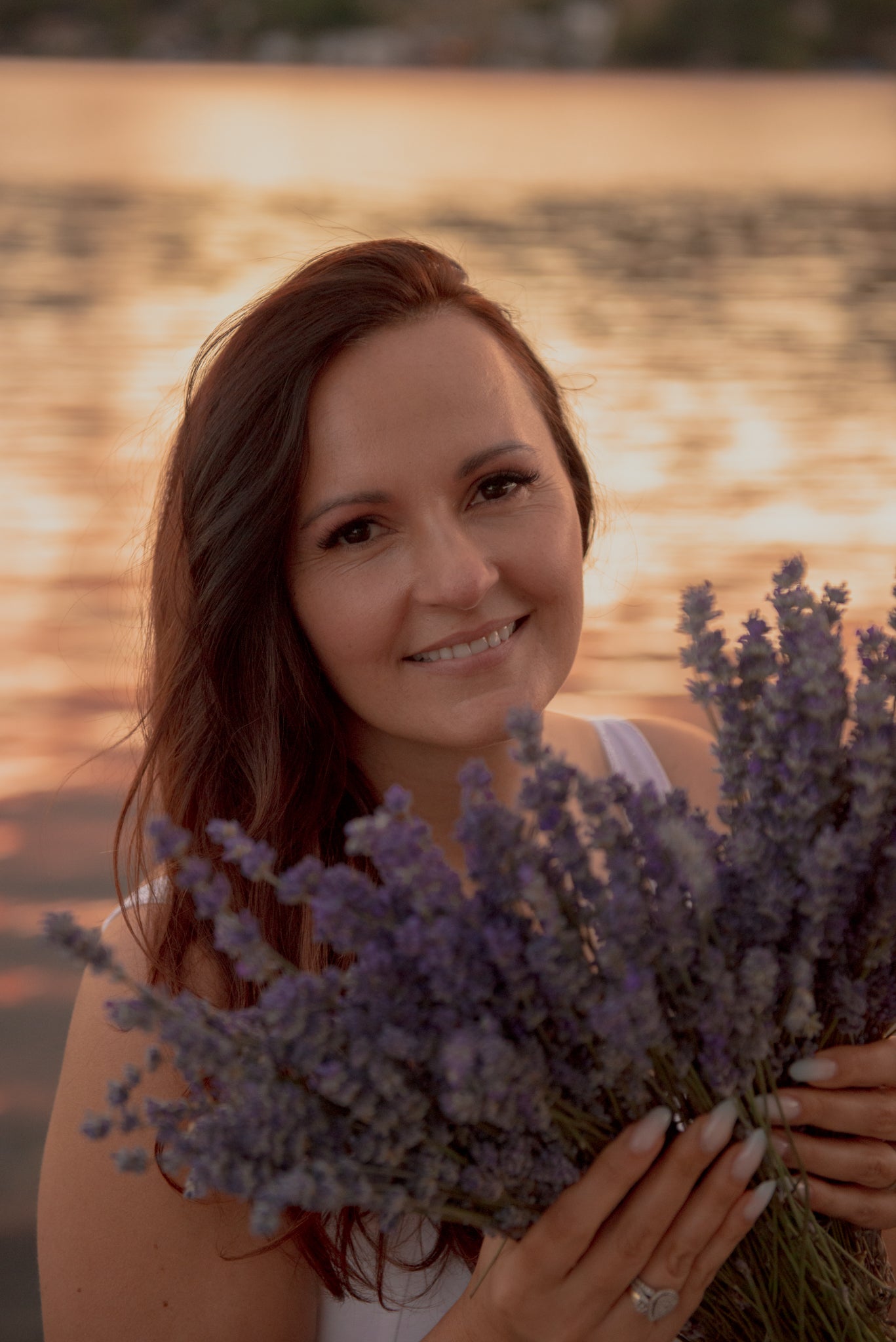 Christina, founder of Mia Noore, holding a bunch of lavender by the lake at sunset in West Kelowna